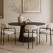 Eettafel Salvator Rond in walnoot met rond blad en getextureerde poot, omgeven door beige stoelen in interieur